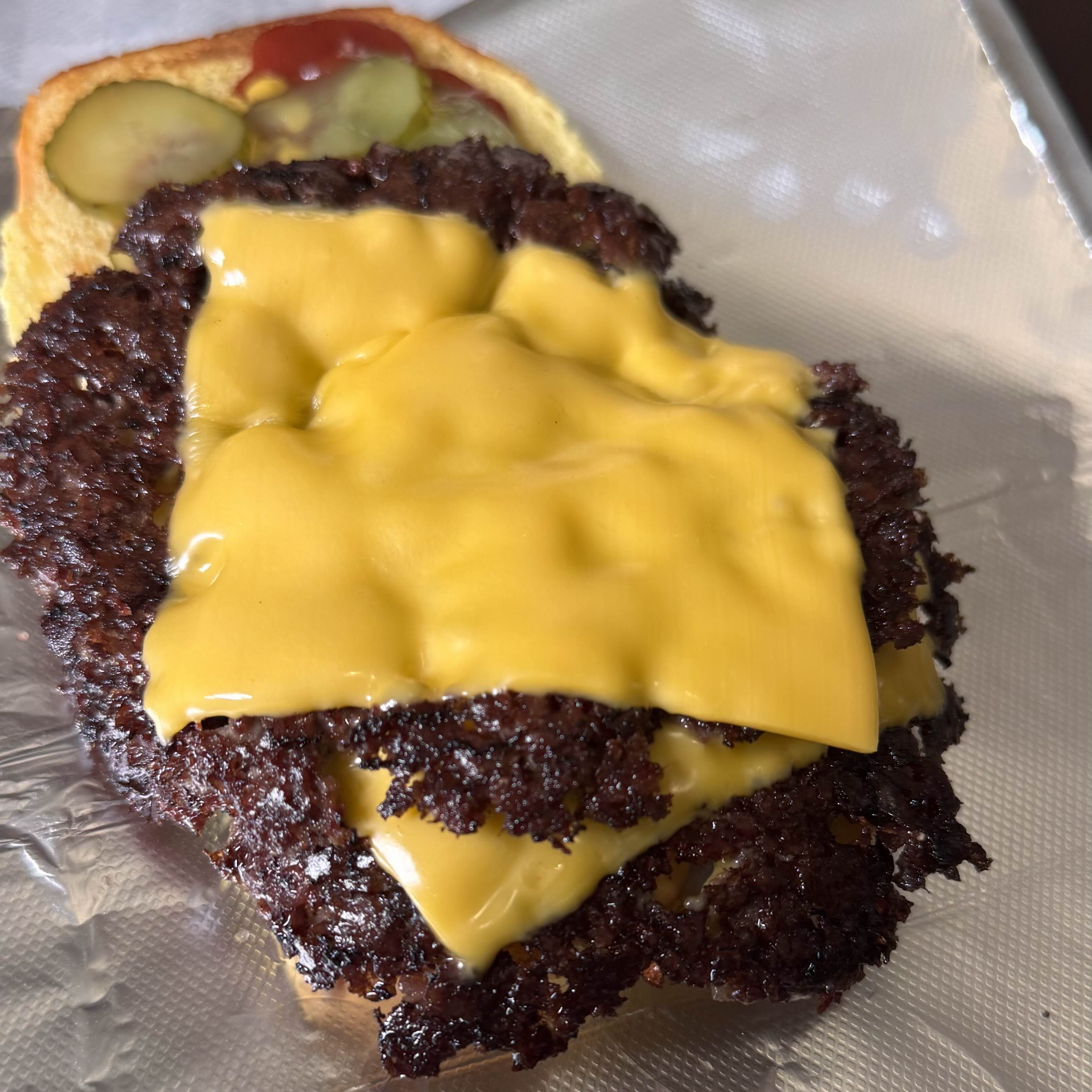 Close-up of a juicy burger with melted American cheese, pickles, and ketchup on a soft bun, resting on foil.